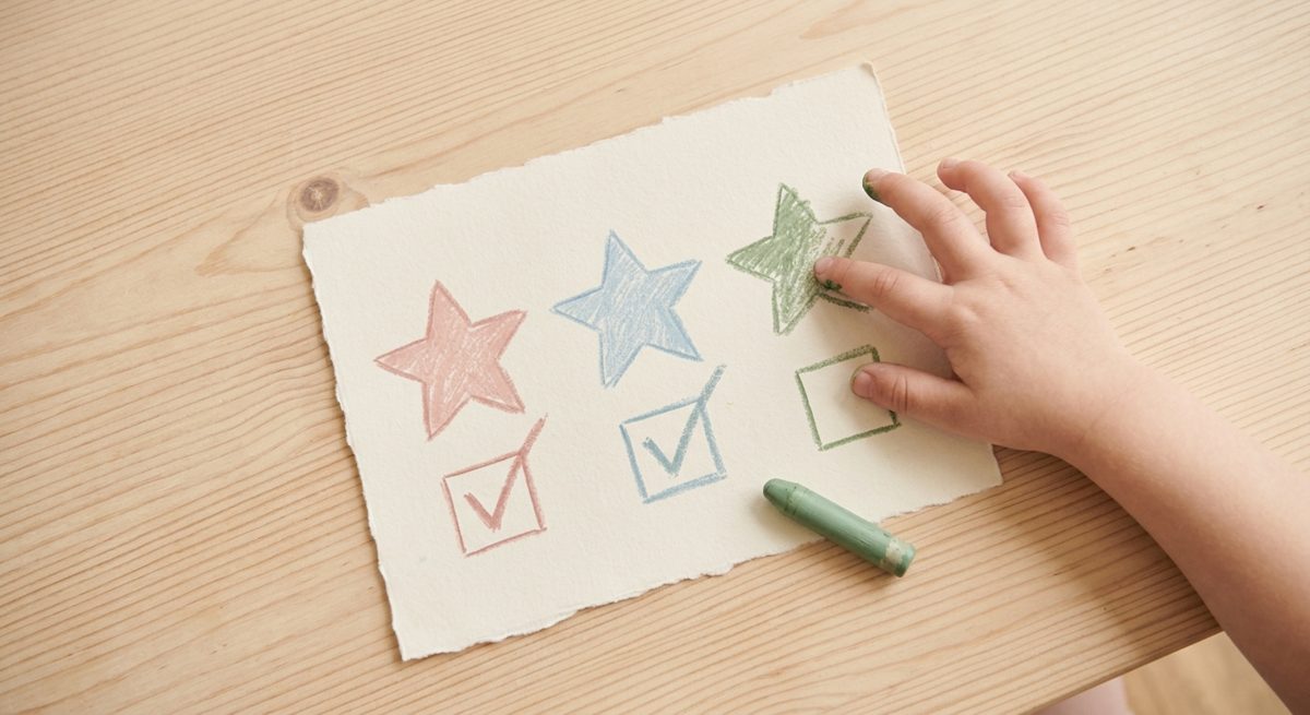 A child colouring in stars on a simple goal chart with tick boxes